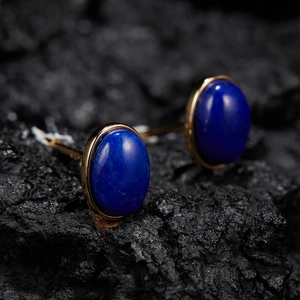 Macro shot of gold-plated oval deep blue jade cufflinks on a dark textured rock background
