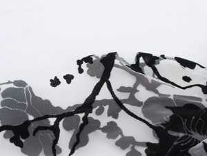 Macro shot of white mesh fabric with black flocked floral patterns and detailed texture