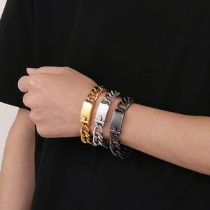 Close-up of three 18k gold-plated and silver thick chain bracelets with metal nameplates