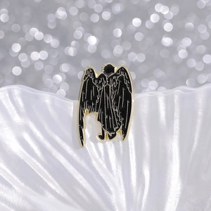 Unique black enamel angel brooch with gold metal wings on a decorative white shell