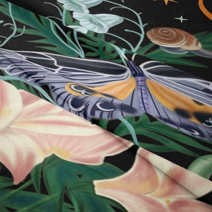 Close-up of tapestry fabric showing detailed dark forest moth and pink lily floral patterns