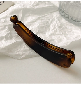 Detailed view of an amber banana hair clip on a minimalist white textured background