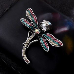 Detailed close-up of a silver dragonfly brooch with colorful rhinestones and faux pearl