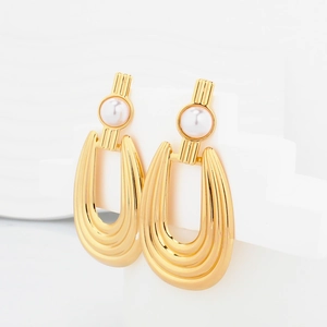Detail of gold U-shaped hoop earrings with vertical texture and white faux pearl accent