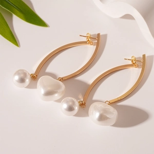 Detail of elegant gold curved earrings with round and heart-shaped faux pearl pendants