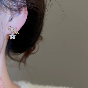 Detail view of gold bow and star drop earrings with sparkling crystals worn by a model