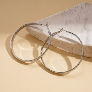 Detailed view of silver hoop earrings with textured geometric design on white stone