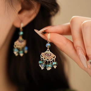 Close-up of vintage gold fan-shaped earrings with purple beads and turquoise tassels