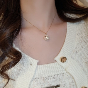 Gros plan d'un collier pendentif perle dorée avec halo de zircons porté par un mannequin