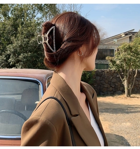 Detail of a large gold metal hair claw with white pearls holding a hair bun securely