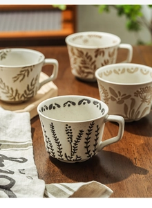 Detail of four ceramic mugs with hand-painted botanical patterns on a rustic wooden table