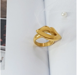 Detail of 18K gold plated lip-shaped statement ring resting on white mesh with pearl