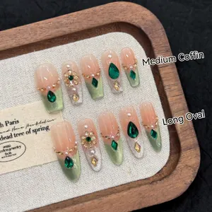 Vintage palace style press-on nails with emerald crystals and gold details on wood tray