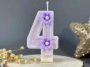 Detail of purple glitter number 4 birthday candle with two 3D flowers on wooden base