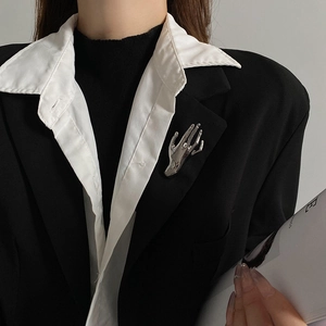 Detailed view of a silver liquid metal hand-shaped brooch on a black blazer jacket