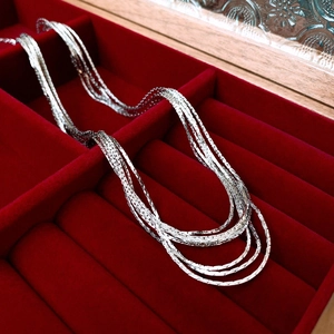 Close-up of layered silver necklace on luxury red velvet background inside a jewelry box