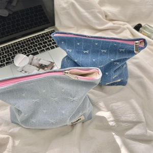 Detail view of denim cosmetic bags with pink zippers and white bow patterns on fabric