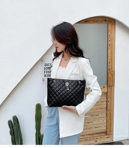Fashionable black quilted tote bag with gold crown charm styled with elegant white blazer
