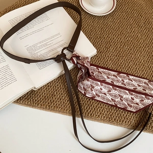 Detail of dark brown leather belt intertwined with red paisley silk scarf on book