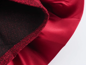 Dettaglio della trama in tweed rosso in contrasto con la fodera in raso liscio di un abito
