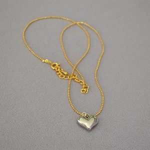 Gold beaded chain necklace featuring a polished silver 3D heart pendant on gray fabric