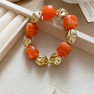 Detailed shot of orange resin beads and irregular golden metal charms on a stylish bracelet
