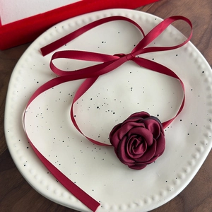 Close-up of burgundy fabric rose necklace with ribbons on decorative white plate