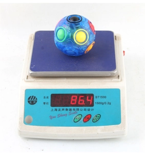 Detailed view of a rainbow puzzle ball toy on a scale showing its weight of 86.4 grams