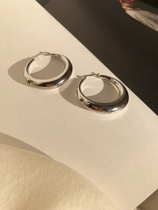 Macro view of thick silver hoop earrings with high-polish finish on white silk background