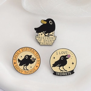 Three creative black enamel crow brooches with humorous text on white textured surface