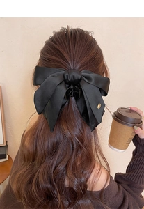 Detail of a large black satin bow hair claw clip worn on wavy brown hair
