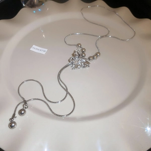 Macro view of silver butterfly necklace with snake chain and polished beads on white ceramic