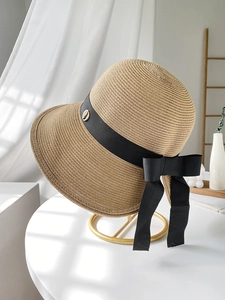 Detailed texture of beige woven straw hat with elegant black ribbon bow and gold buckle