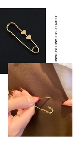 Detail of a gold metal waist pin featuring two delicate heart charms on fabric