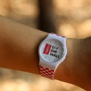 White casual analog watch with red checkerboard strap pattern worn on wrist in daylight
