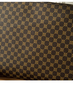 Macro shot of dark brown leather texture with golden clover pattern and litchi grain