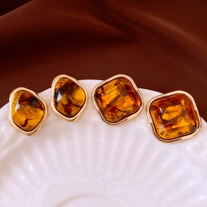 Close-up of amber resin earrings with gold edges on white ceramic and velvet