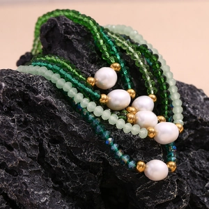 Detail of green crystal beads and freshwater pearl necklace on black natural mineral rock