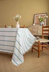 Detail of off-white linen tablecloth with blue stripes and decorative fringed edges