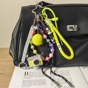Dettaglio portachiavi in corda giallo neon con pallina da tennis su borsa in pelle nera