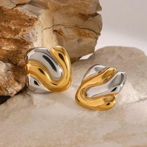 Gros plan de boucles d'oreilles vagues bicolores or et argent sur un socle en pierre