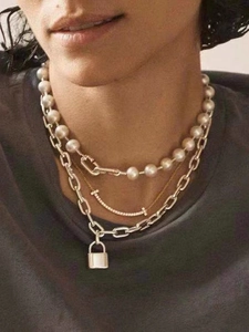 Detail of layered necklace set with pearls, a smile pendant, and a metallic padlock charm