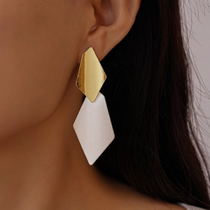Detailed close-up of geometric diamond earrings with brushed silver and gold finish on model