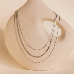 Close-up of triple-layered silver snake chains draped over a minimalist ceramic vase