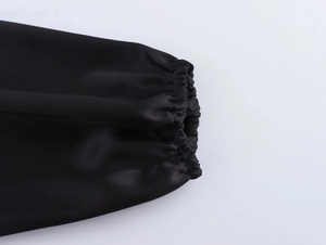Detailed view of elastic cuffs on a black satin long-sleeved dress with smooth texture