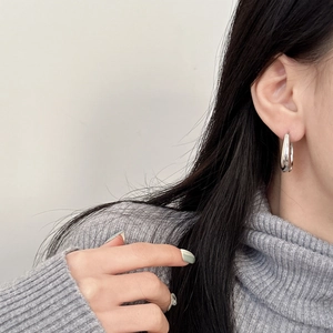 Close-up of minimalist silver hoop earring worn by a model on a grey background