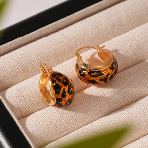 Close-up of golden hoop earrings with leopard print enamel on a soft beige jewelry box