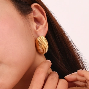 Macro shot of 18K gold plated oval textured earrings worn by a model on a pink background