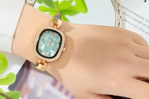 Close-up of women's gold watch with green marble dial and leather strap on wrist