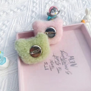 Close-up of metal safety pins on back of pink and green plush cat brooches